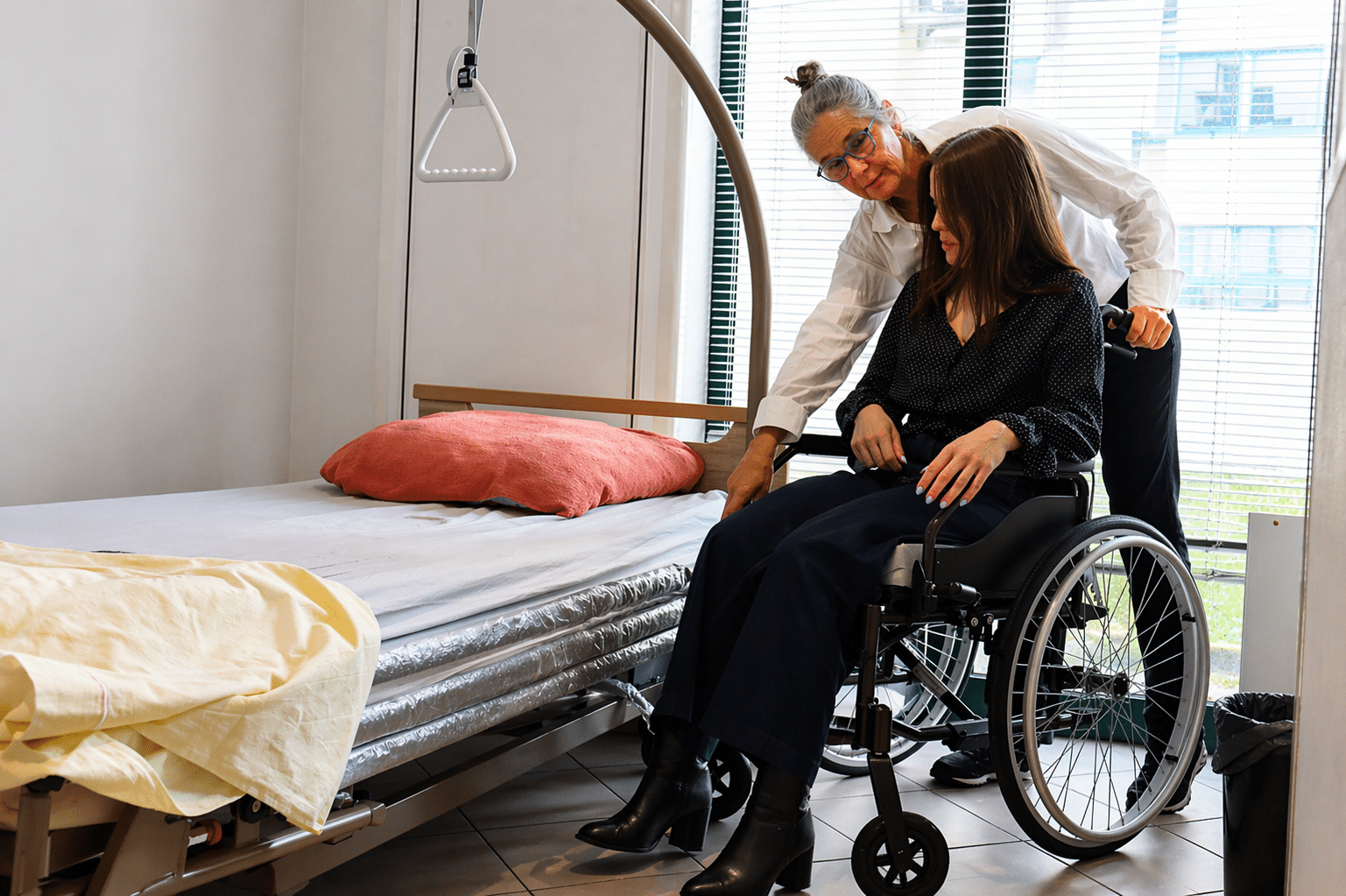 Aide à domicile aidant une personne en fauteuil roulant à se mettre au lit