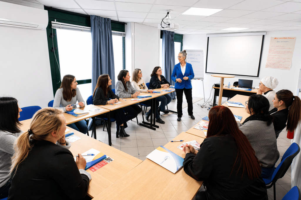 Stagiaires assis dans une salle de formation écoutant la formatrice debout au milieu d'eux